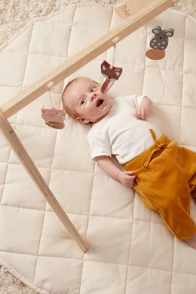 Un bébé allongé sur un nappe admirant les jouets suspendus à une arche d'éveil