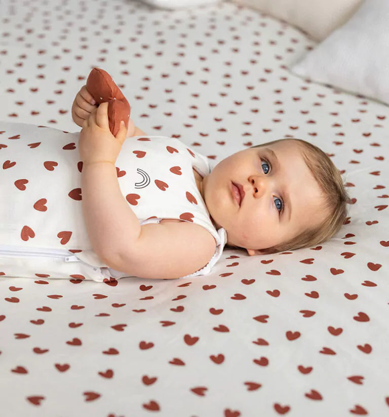 Un bébé allongé sur un lit vêtit d'une gigoteuse || Babykare.fr 