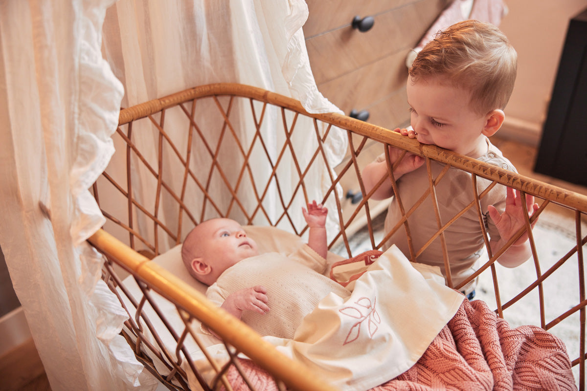 Bébé dans son berceau, équipé d'une gigoteuse et surveillé par son grand frère